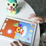Dziecko bawi się na tablecie, grając w gry dla 5 latka na telefon. Na ekranie widać kolorową postać i elementy gry.