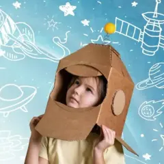 Dziecko w kartonowym hełmie astronauty patrzy w górę, otoczone rysunkami rakiet i planet. To właśnie takie marzenia o kosmosie napędzają nas do odkrywania.