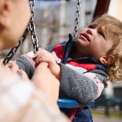 Dziecko na huśtawce trzyma się rączek starszej osoby. To piękne przykłady czynności samoobsługowych i wspólnego spędzania czasu.