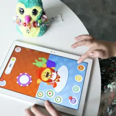 Dziecko bawi się na tablecie, grając w gry dla 5 latka na telefon. Na ekranie widać kolorową postać i elementy gry.