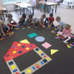 Dzieci w przedszkolu tworzą obrazki z kolorowych figur geometrycznych.