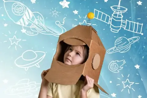 Dziecko w kartonowym hełmie astronauty patrzy w górę, otoczone rysunkami rakiet i planet. To właśnie takie marzenia o kosmosie napędzają nas do odkrywania.