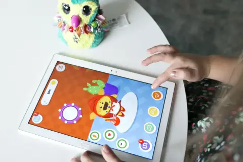 Dziecko bawi się na tablecie, grając w gry dla 5 latka na telefon. Na ekranie widać kolorową postać i elementy gry.