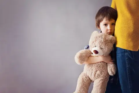 Smutne dziecko płacze, tuląc misia, gdy mama wychodzi.