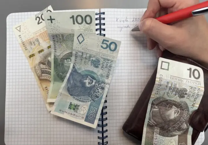 Zapisywanie wydatków na dziecko z orzeczeniem o potrzebie kształcenia specjalnego. Na zeszycie leżą banknoty 200, 100, 50, 10 zł.