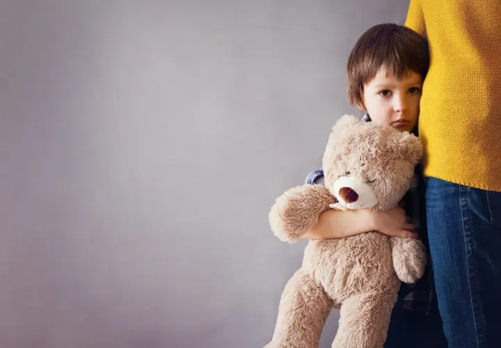 Smutne dziecko płacze, tuląc misia, gdy mama wychodzi.