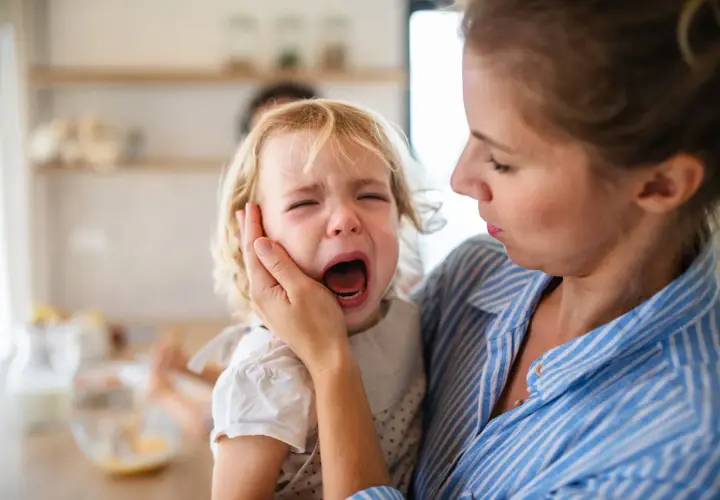 Mama próbuje uspokoić dwulatka, który przeżywa histerię. Dziecko głośno płacze, mama trzyma je czule.