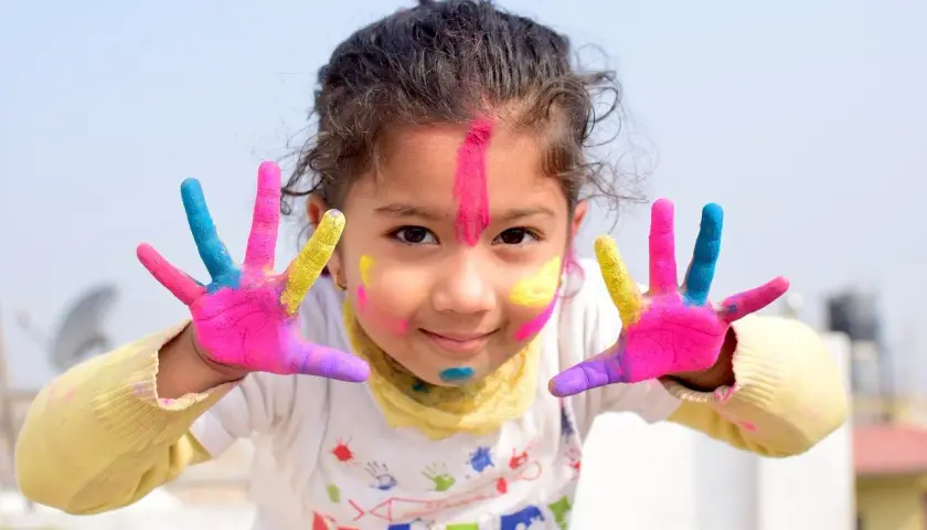 Radosna dziewczynka z kolorowymi dłońmi i twarzą, gotowa do urodzinowych zabaw.
