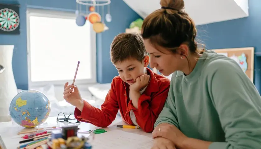 Mama z synem uczą się w domu. Czy edukacja domowa jest płatna? Na biurku globus, kredki i książki.