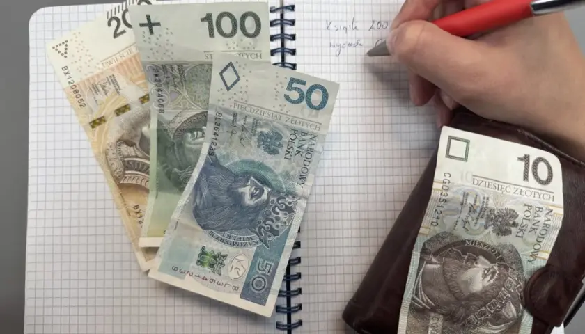 Zapisywanie wydatków na dziecko z orzeczeniem o potrzebie kształcenia specjalnego. Na zeszycie leżą banknoty 200, 100, 50, 10 zł.