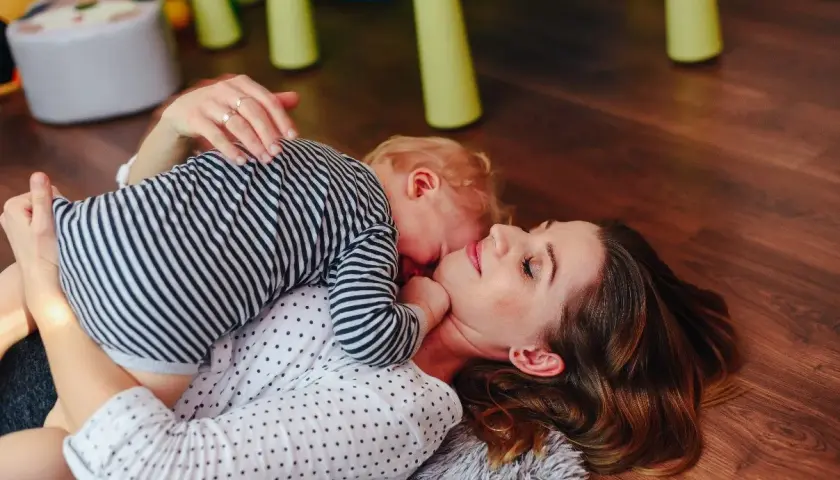 Mama i dziecko leżą na podłodze. Dziecko przytula się do mamy. To piękny przykład, co to stymulacja rozwoju poprzez bliskość i zabawę.