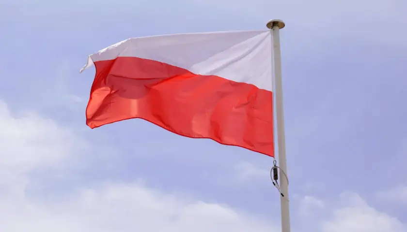 Biało-czerwona flaga powiewa na maszcie. Duma i symbole narodowe Polski w błękitnym niebie.