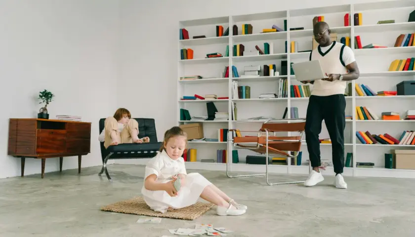 Przytulny gabinet logopedyczny z regałami pełnymi książek. Dzieci bawią się kartami, a logopeda z laptopem czuwa.