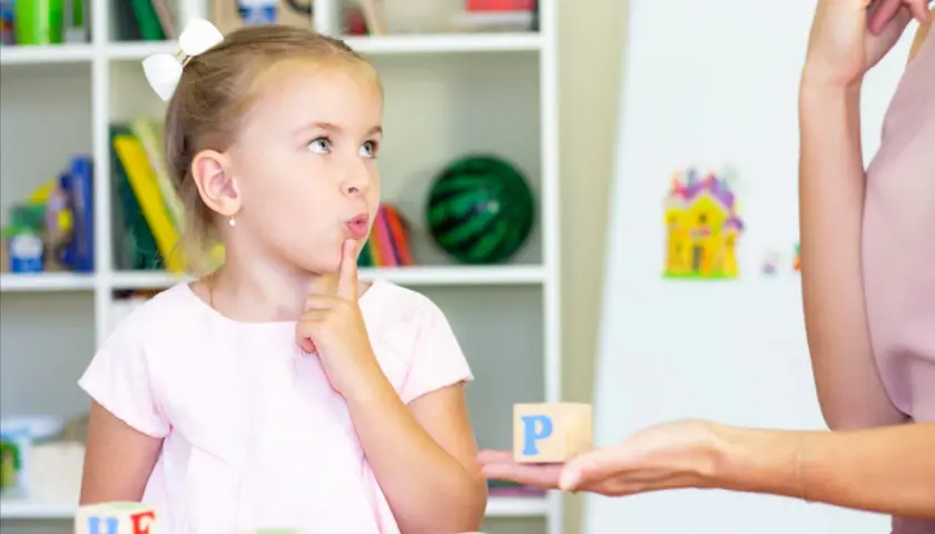 Dziewczynka z palcem przy ustach myśli podczas zabawy edukacyjnej z literkami.