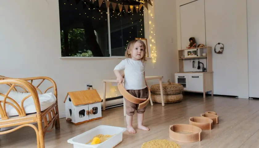 Dziecko bawi się w pokoju inspirowanym 10 zasadami Montessori. Drewniane zabawki, domek i kuchnia zachęcają do samodzielnej nauki.
