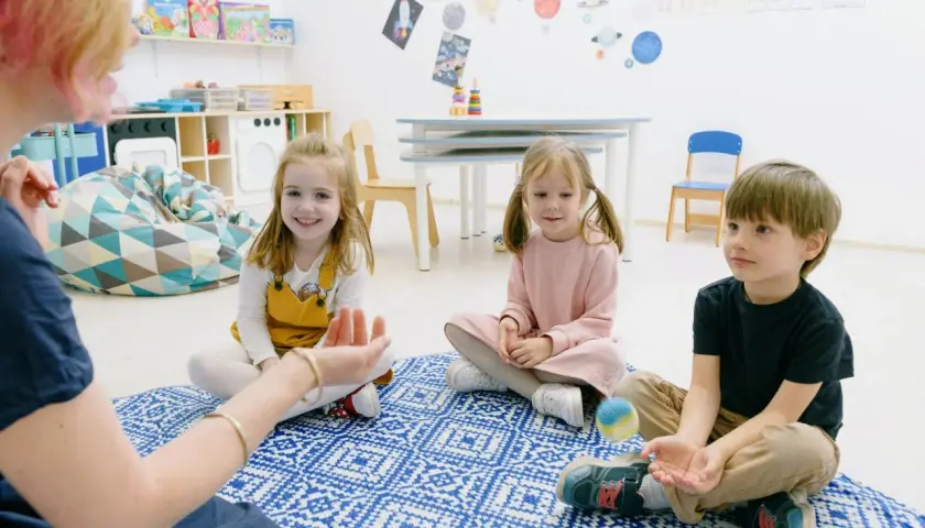 Dzieci biorą udział w zabawach integracyjnych w przedszkolu, siedząc na dywanie i słuchając nauczycielki.