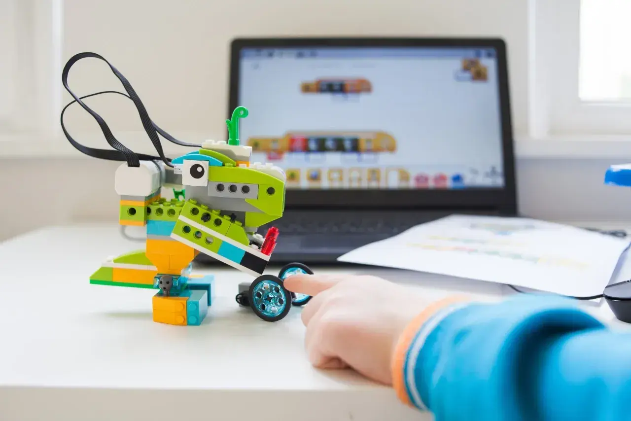 Dziecko buduje robota z klocków, ucząc się programowania. Komputer pokazuje interfejs do tworzenia kodu dla robotów w edukacji.