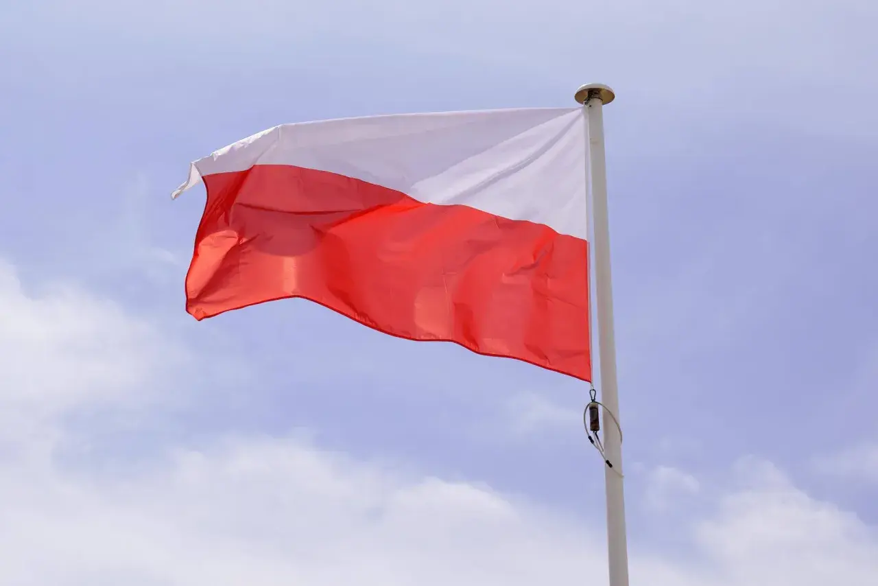 Biało-czerwona flaga powiewa na maszcie. Duma i symbole narodowe Polski w błękitnym niebie.