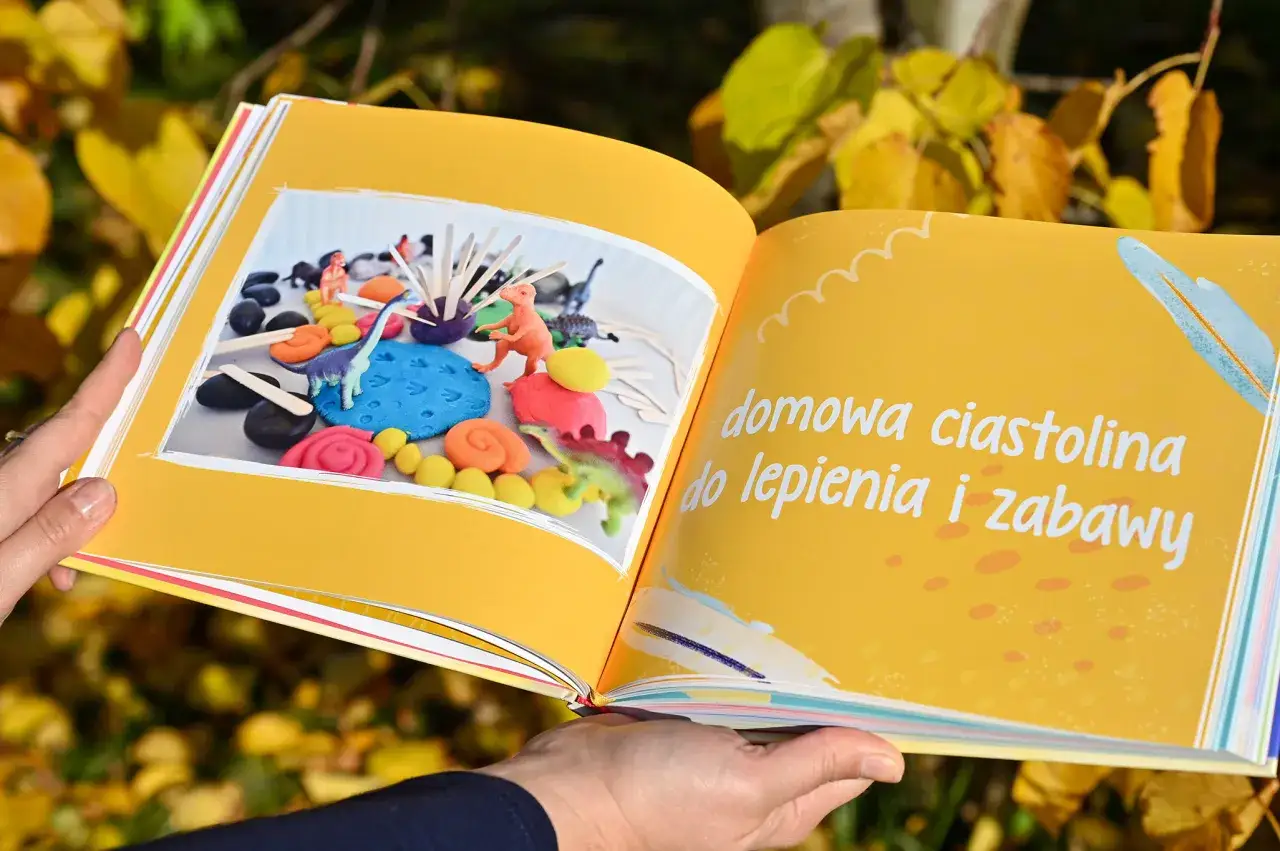 Otwarta książka z kolorowymi dinozaurami i masą plastyczną, idealna do nauki, jak wydać książkę dla dzieci.