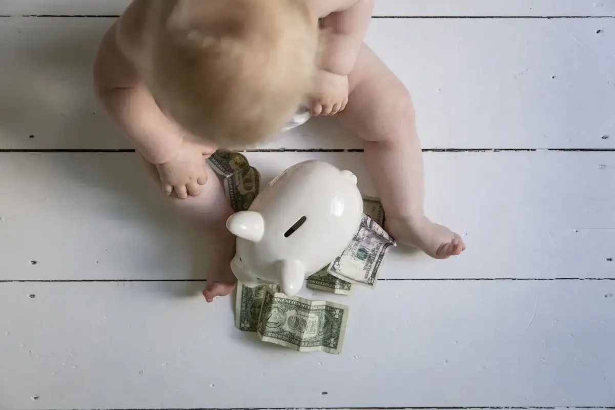 Niemowlę z skarbonką i banknotami. Początki edukacji finansowej dzieci.