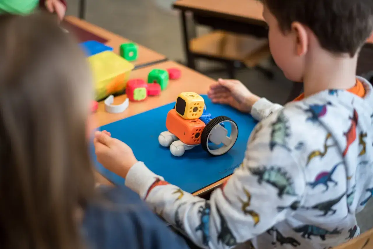 Dzieci budują i programują roboty w edukacji. Kolorowe klocki i mały pojazd na niebieskiej macie.